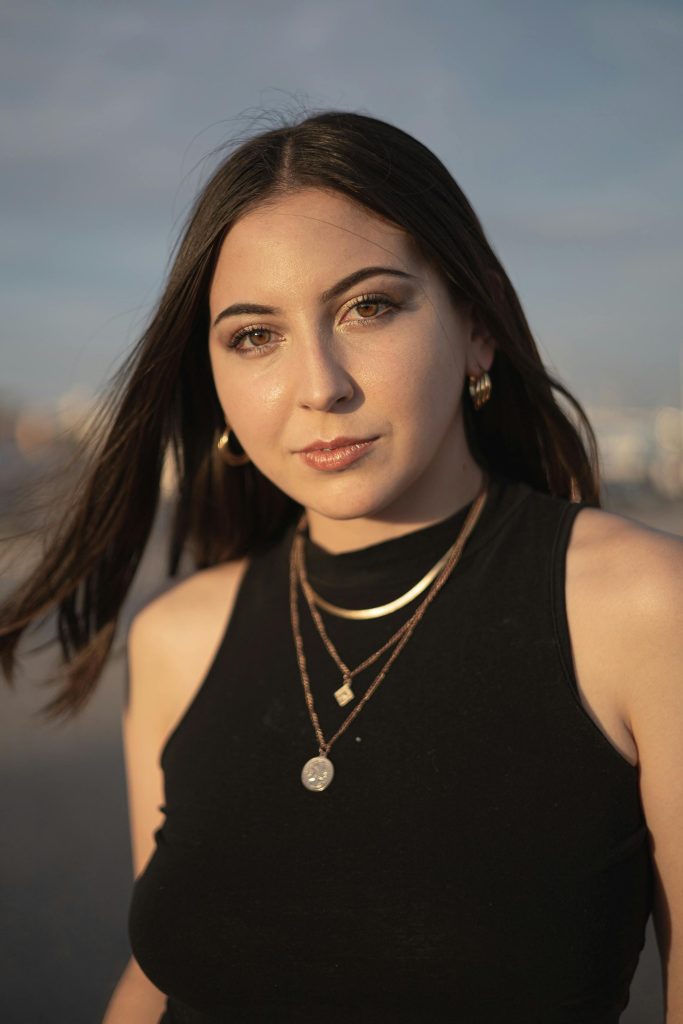 pexels-photo-16346891-16346891 Portrait of a young woman with jewelry, black crop top, and windblown hair at sunset.